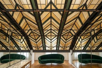 Verrière Art Déco en fer forgé et vitraux géométriques ambrés installée dans un salon parisien avec parquet en chevrons et canapé en velours vert émeraude