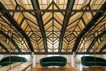 Verrière Art Déco en fer forgé et vitraux géométriques ambrés installée dans un salon parisien avec parquet en chevrons et canapé en velours vert émeraude